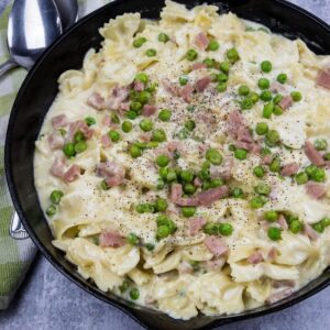 Farfalle pasta with ham and peas in a creamy sauce in a large cast iron skillet.