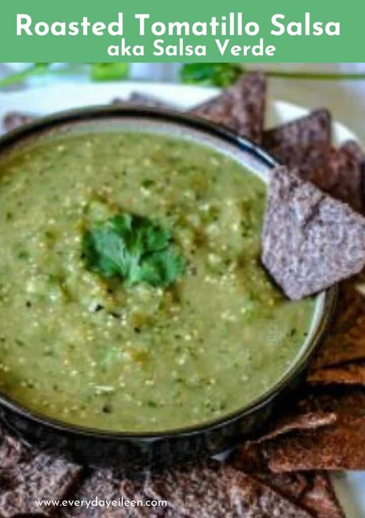 salsa verde in a brown bowl. A blue chip tortilla is stuck in the side of the bowl. Fresh cilantro in the center of the bowl.