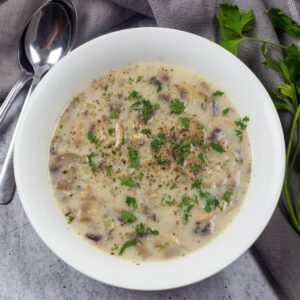 a white soup bowl filled with creamy broth, sliced mushrooms, and topped with chopped parsley.