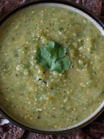 A brown bowl filled with salsa verde and topped with a cilantro leaf.
