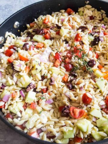 A large black pan holding a batch of Greek orzo pasta salad recipe