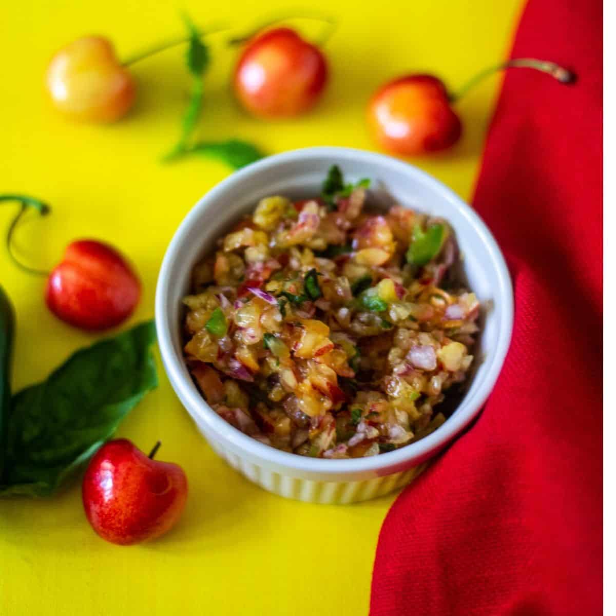 Cherry salsa in a white bowl with cherries and mint on the side of the bowl