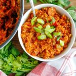 A white bowl filled with jambalaya and cauliflower rice topped with chopped green onions and a bunch of fresh parsley on the side.