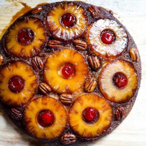 An overhead view of a pineapple upside down cake topped with pineapple slices, pecans, and maraschino cherries.