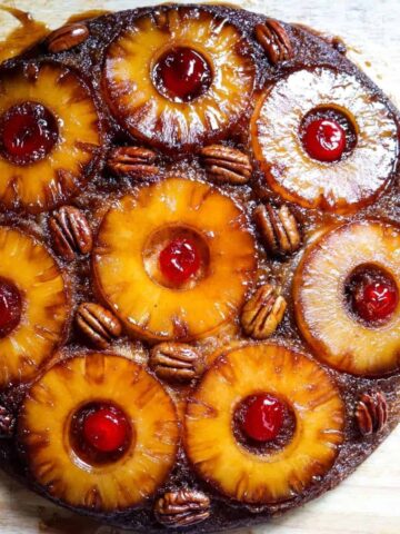 An overhead view of a pineapple upside down cake topped with pineapple slices, pecans, and maraschino cherries.