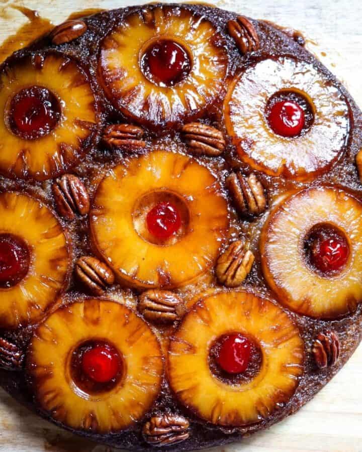 An overhead view of a pineapple upside down cake topped with pineapple slices, pecans, and maraschino cherries.