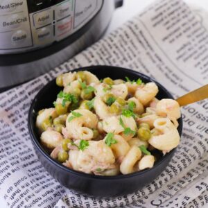 A black bowl with spiral pasta, peas, and tuna on a linen napkin.