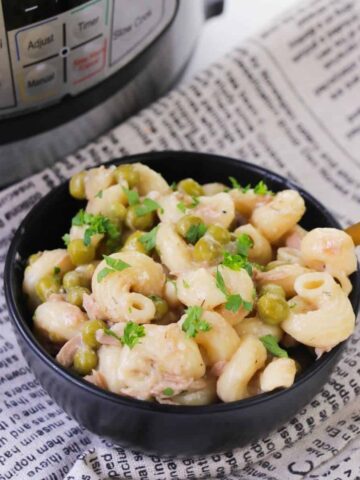 A black bowl with spiral pasta, peas, and tuna on a linen napkin.