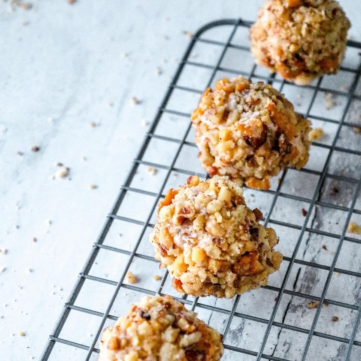 A row of keto fat bombs covered with crushed pecans on a wire rack.