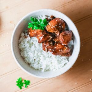 A bowl of white rice topped with Korean BBQ chicken and white sesame seeds