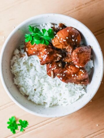 A bowl of white rice topped with Korean BBQ chicken and white sesame seeds
