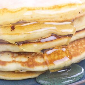 A stack of fluffy buttermilk pancakes dripping with maple syrup.