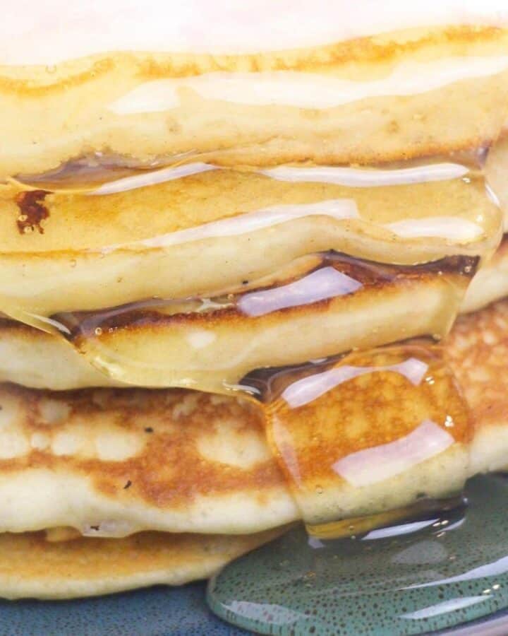 A stack of fluffy buttermilk pancakes dripping with maple syrup.