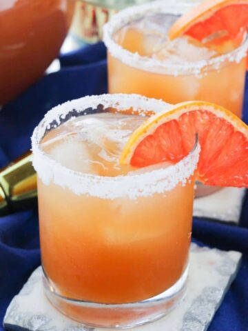 A clear glass filled with grapefruit margarita with salt rimming the glass.