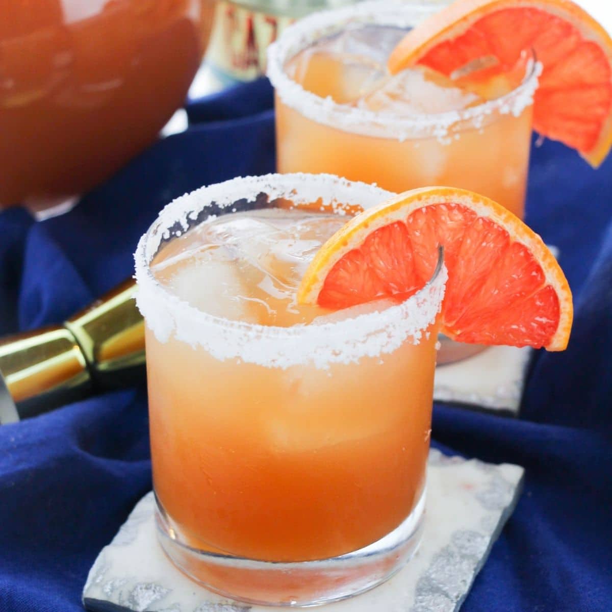A clear glass filled with grapefruit margarita with salt rimming the glass.