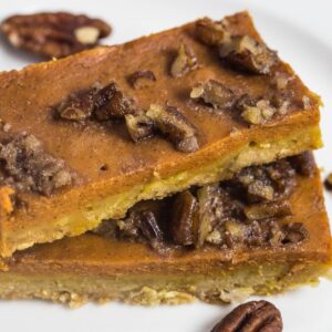 Pumpkin pie bar topped with candy pecans on a white plate