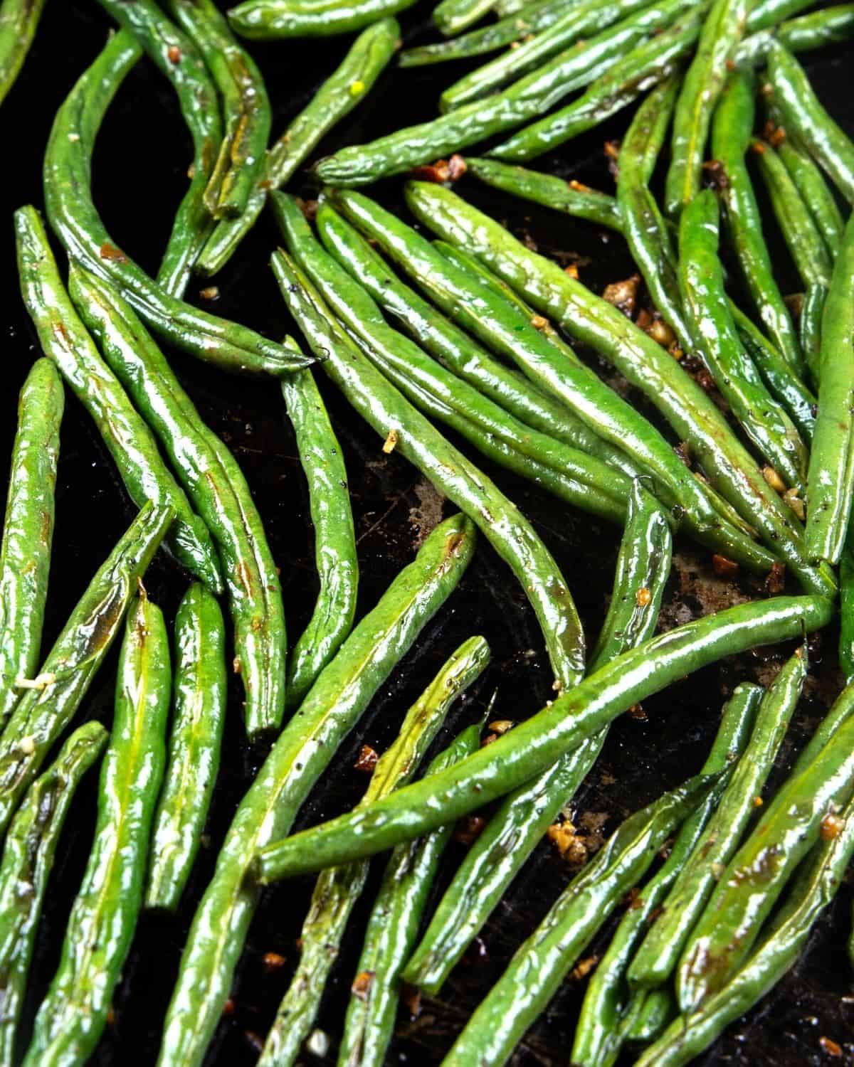 Oven roasted green beans on a baking sheet sprinkled with salt, pepper, and fresh garlic. 