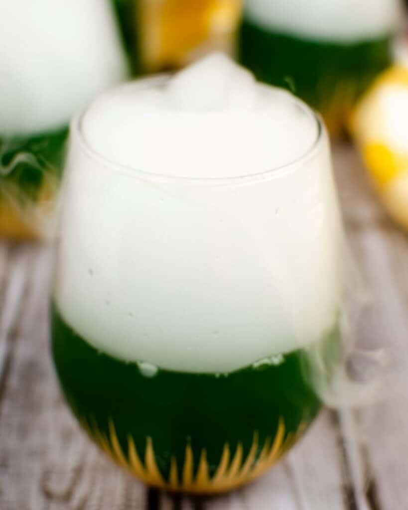 A smoldering green Halloween cocktail with dry ice smoking from the top of the glass.