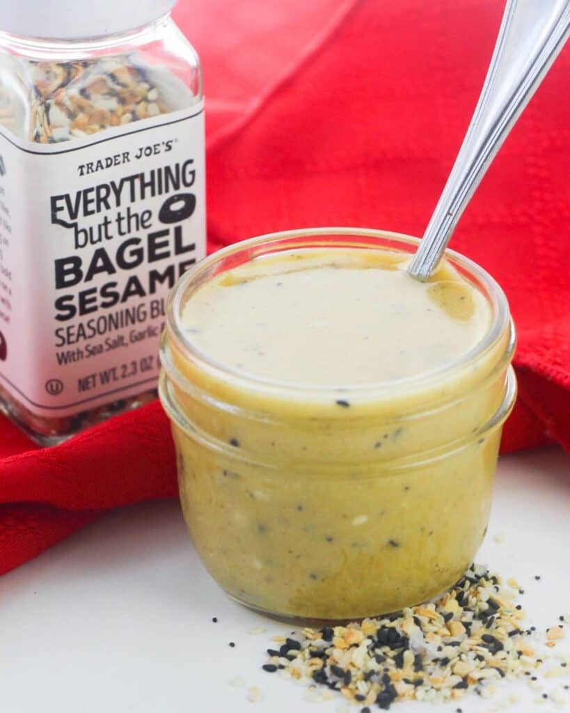 A bowl of everything bagel salad dressing with a bottle of seasoning behind it.