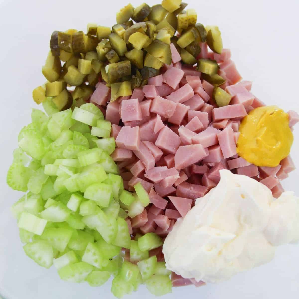 Diced ham, pickles, celery, mayo, mustard in a bowl to make homemade ham salad.