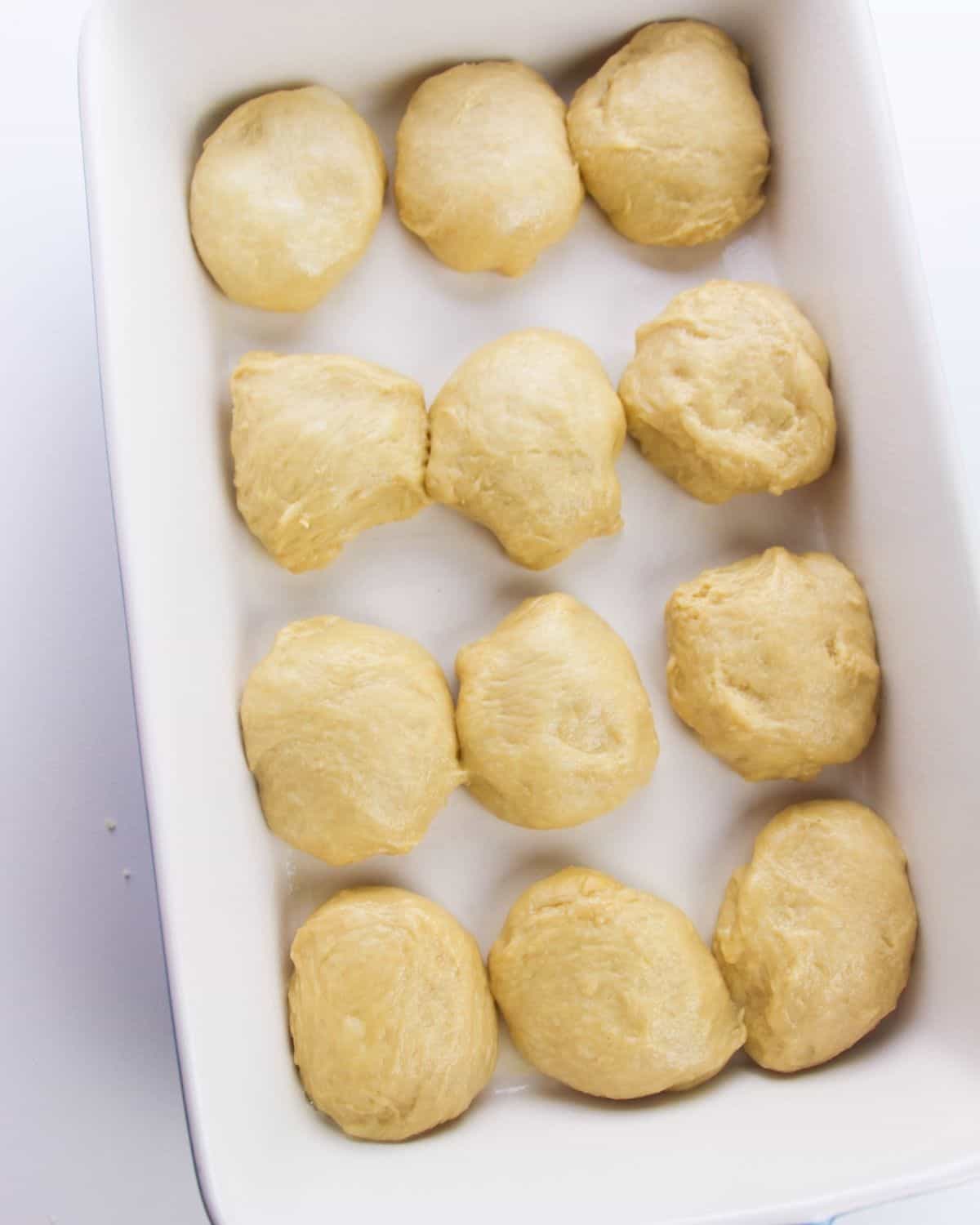 Unbaked rolls in a white baking dish to proof and double in size.