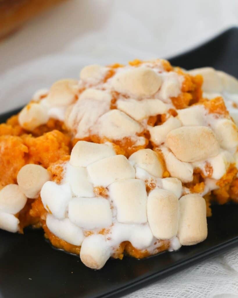 Sweet potato casserole topped with marshmallows on a black plate. 