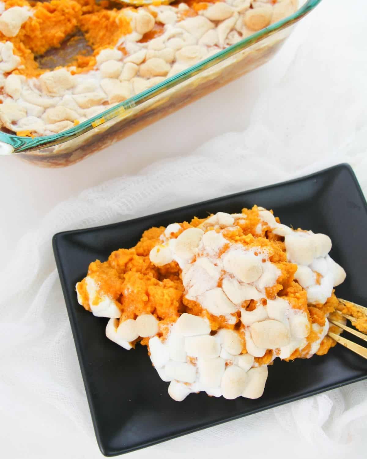 A black plate with mashed sweet potatoes topped with marshmallows