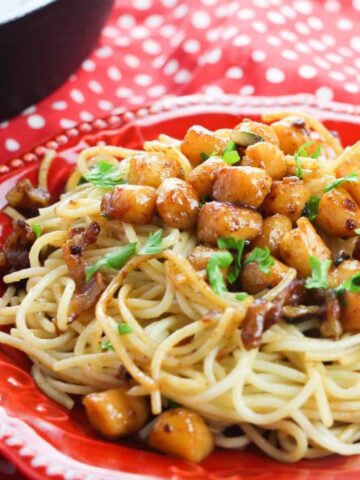 A red dinner plate topped with scallops pasta with a brown butter.
