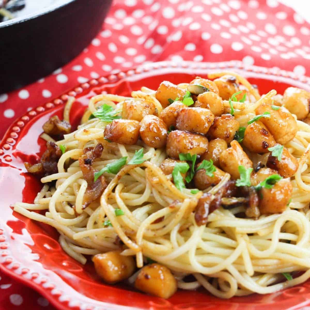 A red dinner plate topped with scallops pasta with a brown butter.