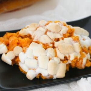 Marshmallow topped sweet potatoes on a black platter.