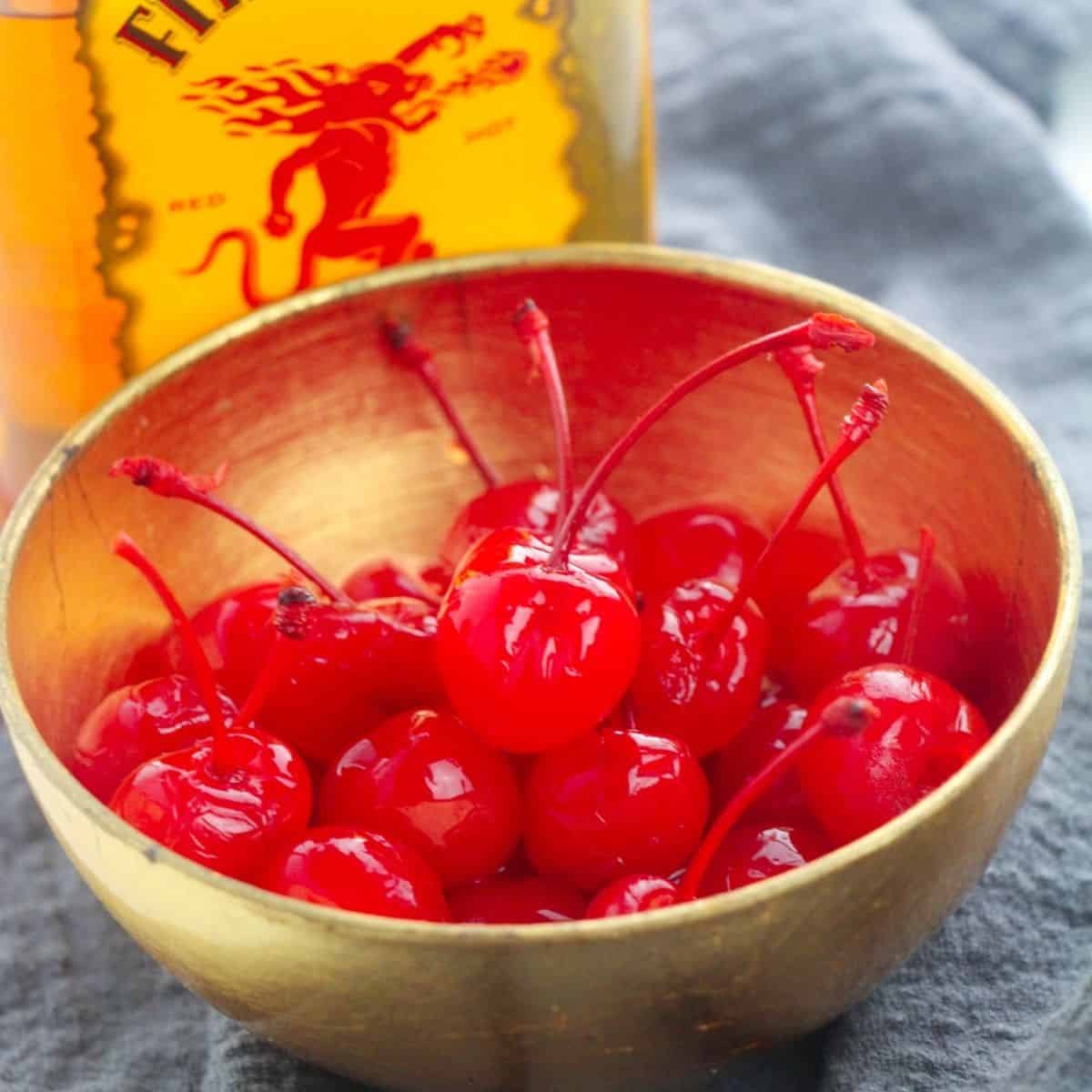 A bowl of cherries with a bottle of fireball whiskey behind it.