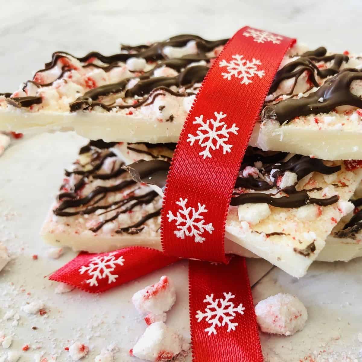 A few pieces of white chocolate peppermint bark wrapped in red ribbon with snow flakes on it.