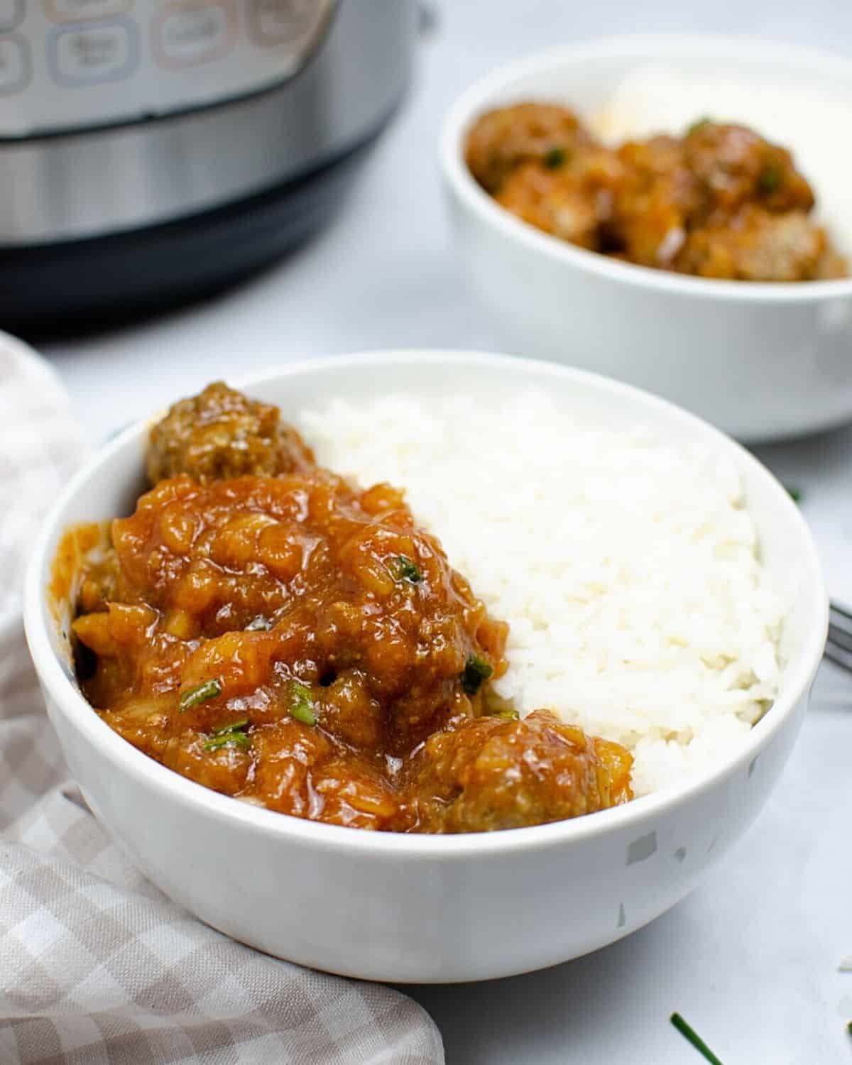 A white bowl with white rice and meatballs in a spicy bbq sauce.