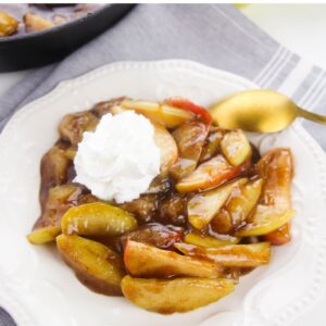 Fried Apples in a white bowl topped with fresh whipped cream.