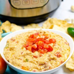 A bowl of Mexican cheese melted in a white bowl topped with tomatoes