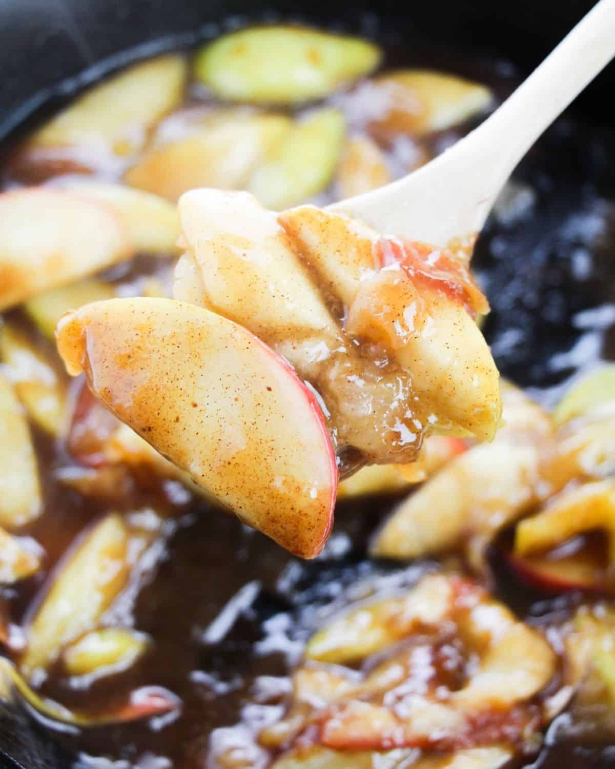 Apples fried in butter and seasoned with apple pie spice on a spoon over a skillet.