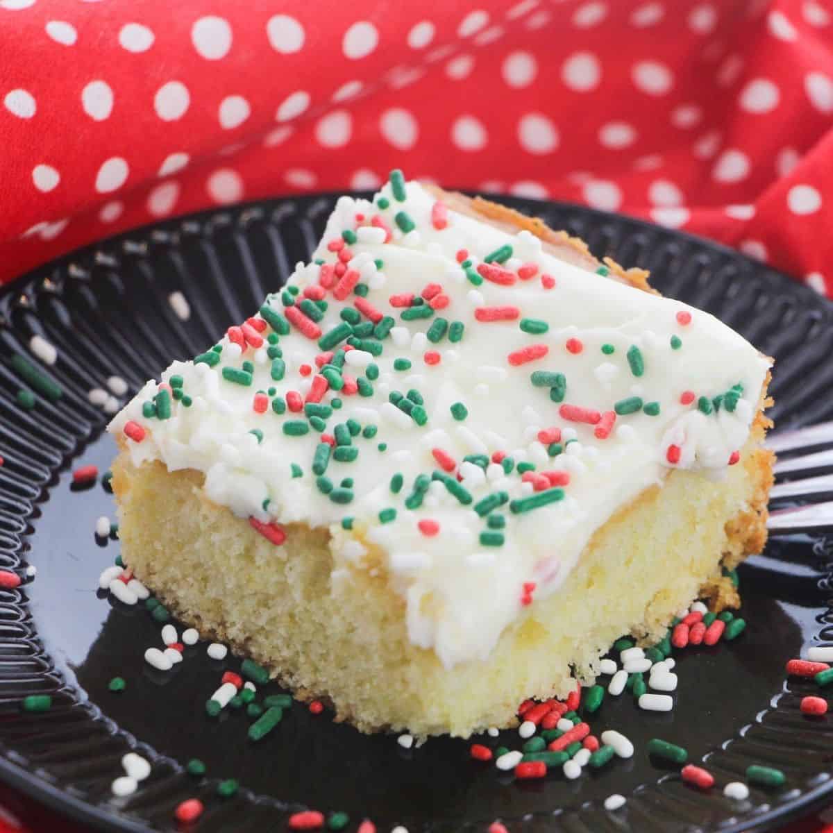 A slice of sugar cookie cake topped with icing and holiday sprinkles