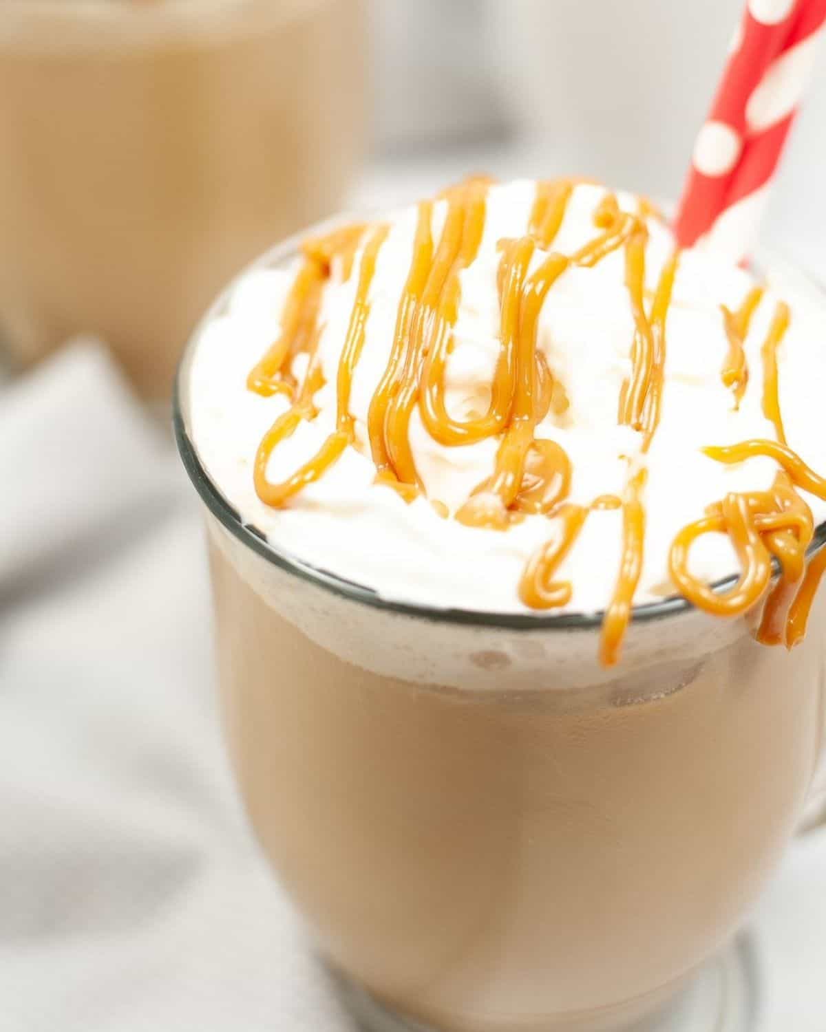 A glass filled with macchiato and topped with whipped cream, caramel and a red polka dot straw in it.