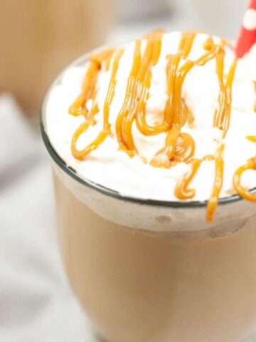 A clear mug filled with latte and topped with whipped cream and drizzled with caramel.