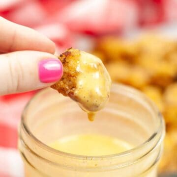 A hand holding a chicken nugget that had been dipped into a yellow sauce.