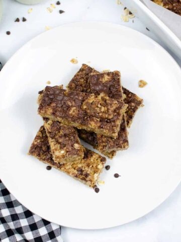 Homemade granola bars stacked on a white plate with a checkerboard napkin next to the plate.