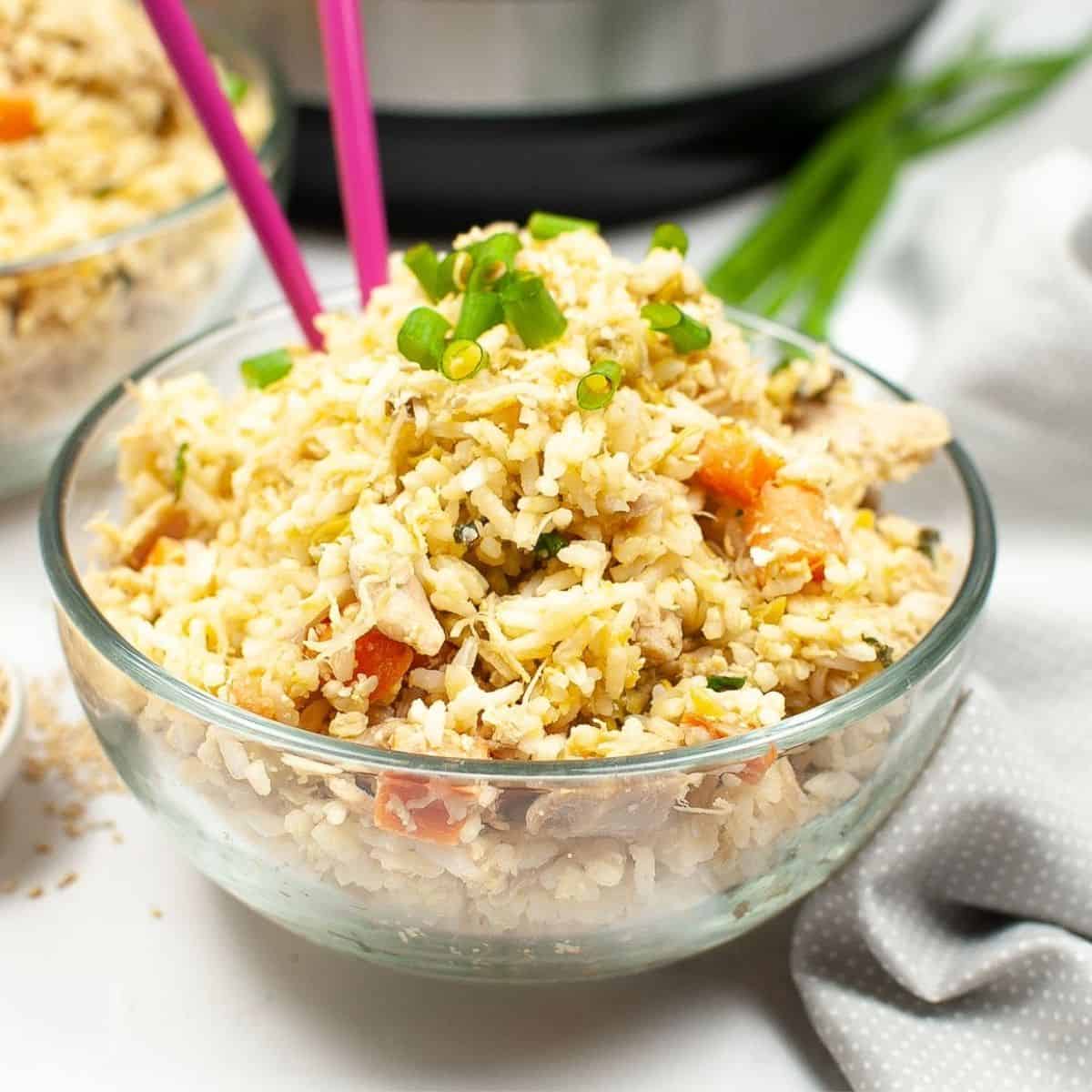 A bowl of rice and shredded chicken with pink chopsticks in the rice.