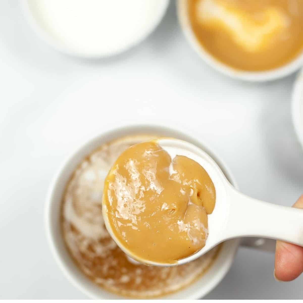Caramel sauce on a Tablespoon over a white coffee cup.