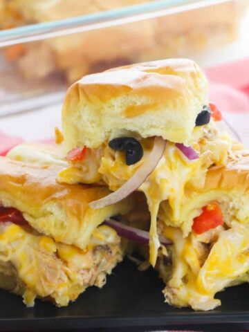 A stack of sliders filled with cheese, chicken. olives, and onions