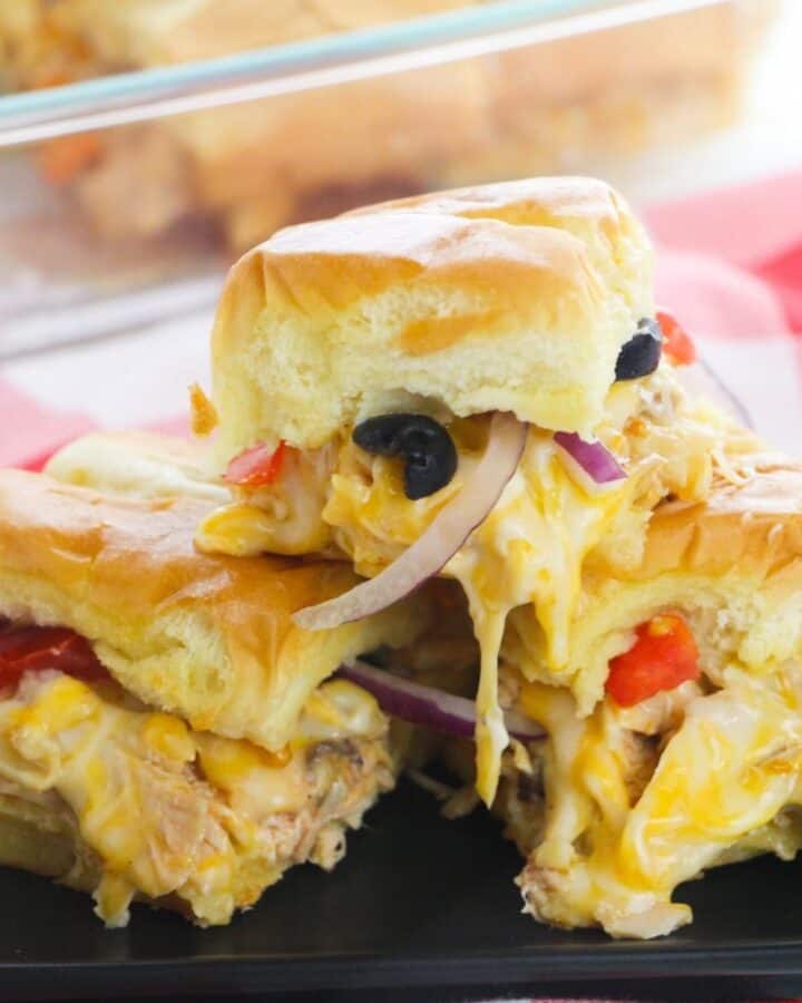 A stack of sliders filled with cheese, chicken. olives, and onions