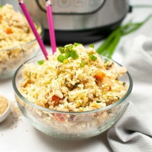 A glass bowl with chicken, rice, and veggies topped with green onion. Pink chopsticks in the bowl.