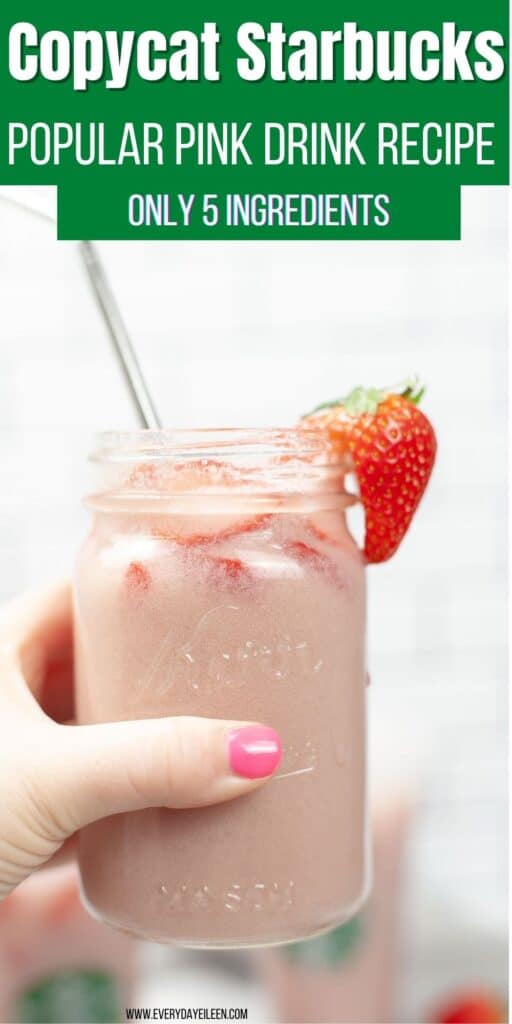 A hand lifting a glass mason jar filled with pink creamy drink, silver straw, and a strawberry on the side of the glass.