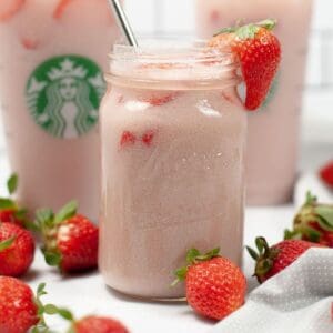 A clear glass mason jar filled with a pink drink copycat drink with a silver straw and a strawberry on the edge of the glass.