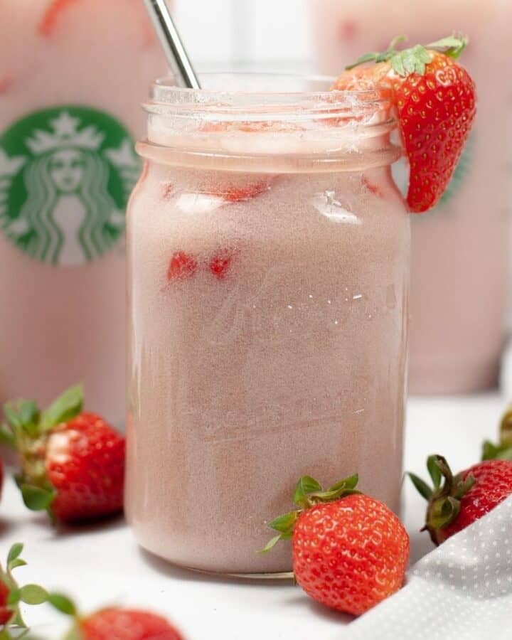 A clear glass mason jar filled with a pink drink copycat drink with a silver straw and a strawberry on the edge of the glass.