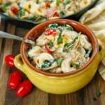 A yellow bowl with creamy tortellini, grape tomatoes, and fresh spinach in it.